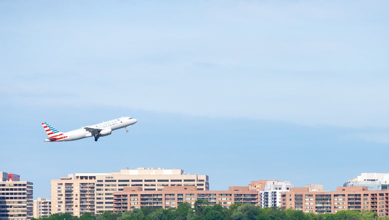 An airplane takes off with a blue sky and buildings in the background