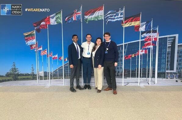 Four Georgetown Fulbrighters stand in front of a large image of countries' flags