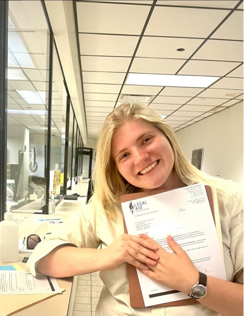 A young woman smiling and holding a file in an office setting.