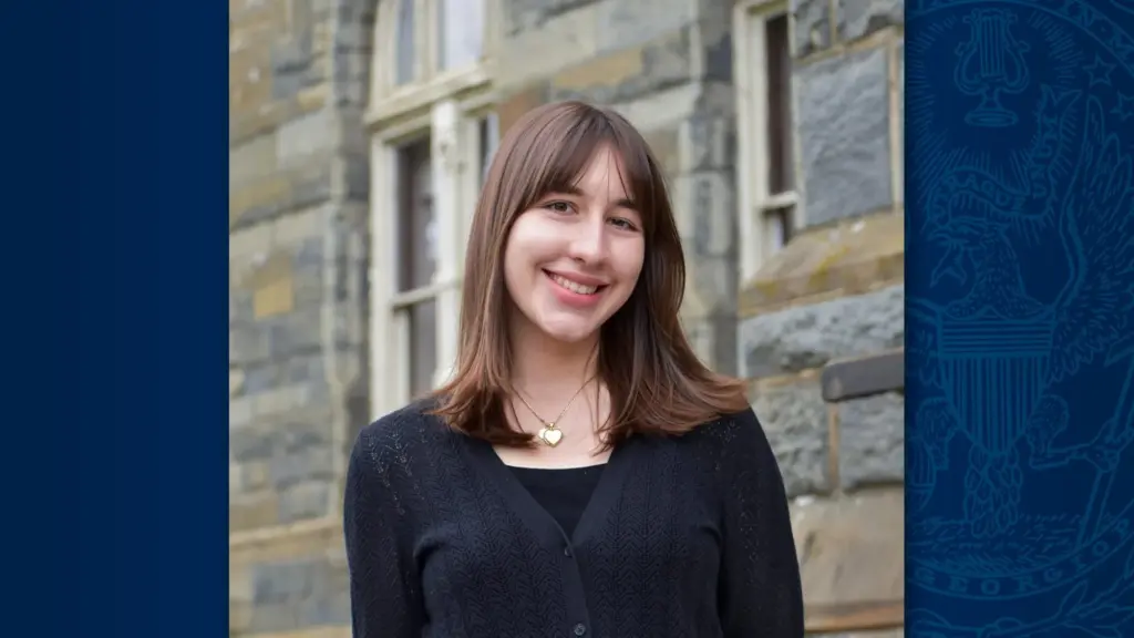 A young woman with brown hair standing in front of Healy Hall and smiling.