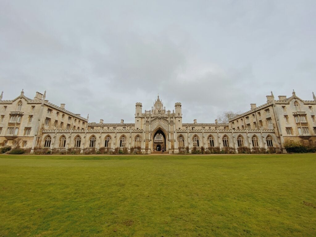 A wide limestone building against a gray sky and green lawn.