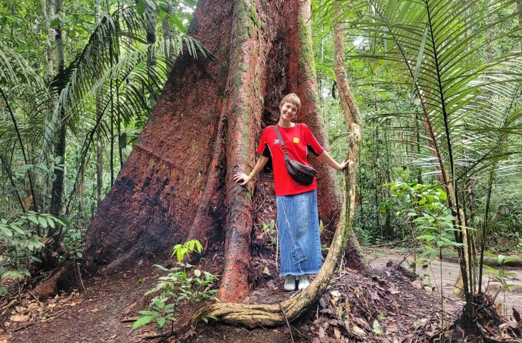 Lexie Meger stands in front of a tree and green foliage