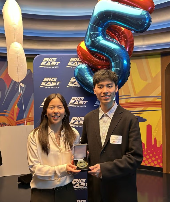Georgetown students in business attire stand in front of large balloons and a blue standing banner with 